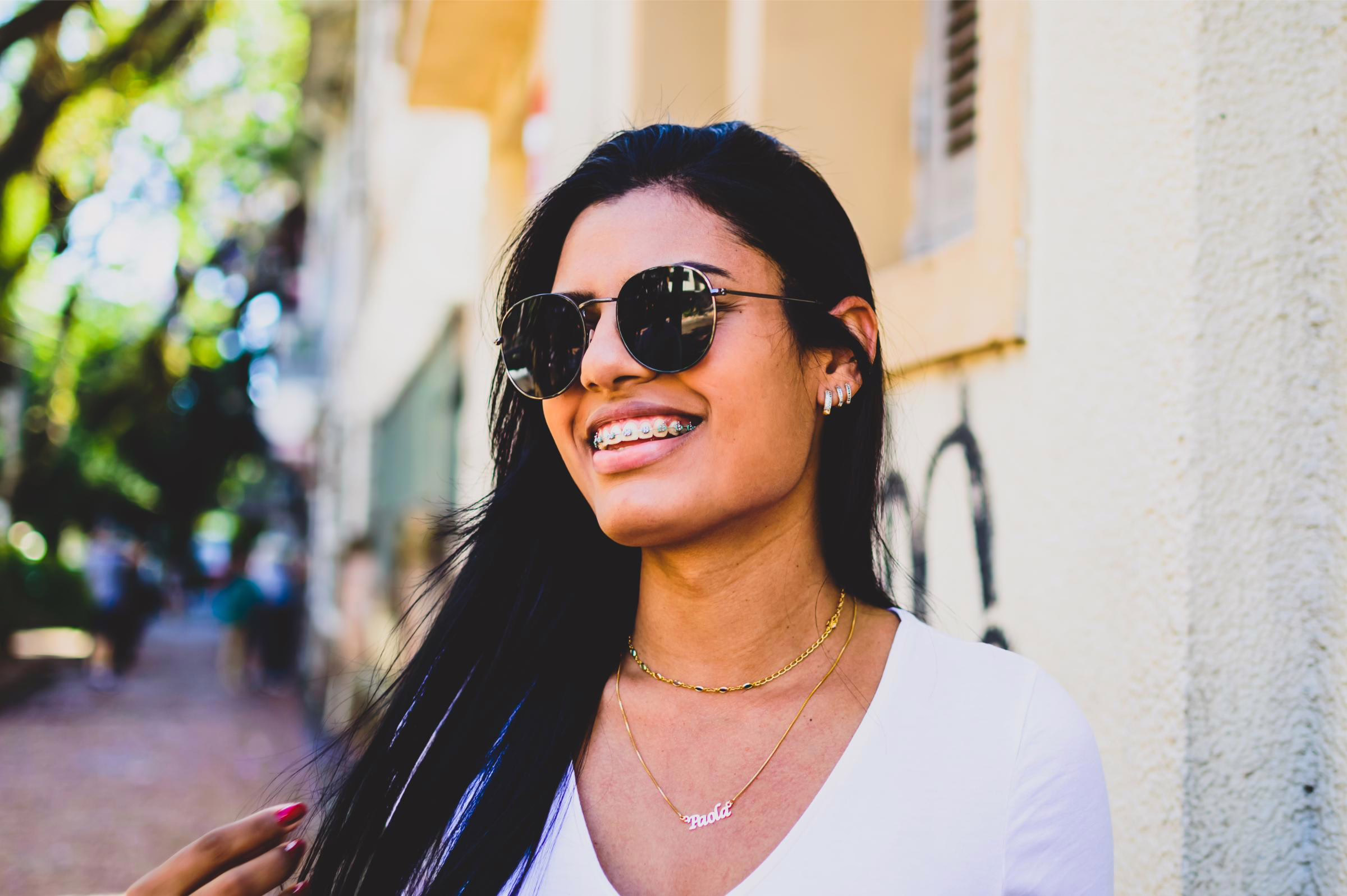 Smiling young woman in sunglasses showing her braces outdoors after orthodontic treatment in Leesburg